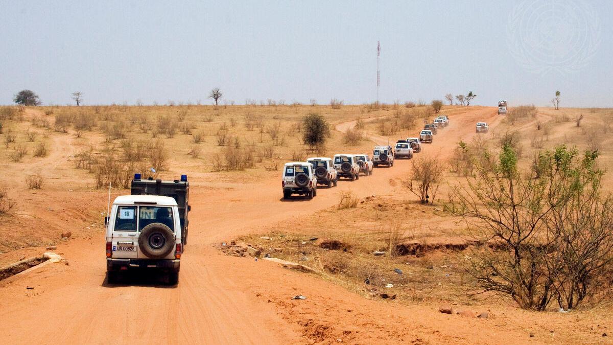 A convoy of UN four wheel drive vehicles along a red dirt road.