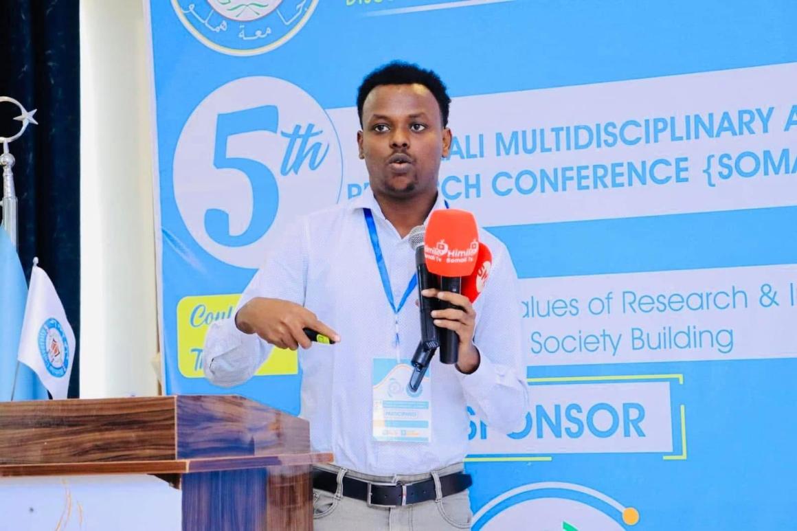 Abdishakur Abdirahman in front of a banner of the 5th Somali Multidisciplinary Research Conference